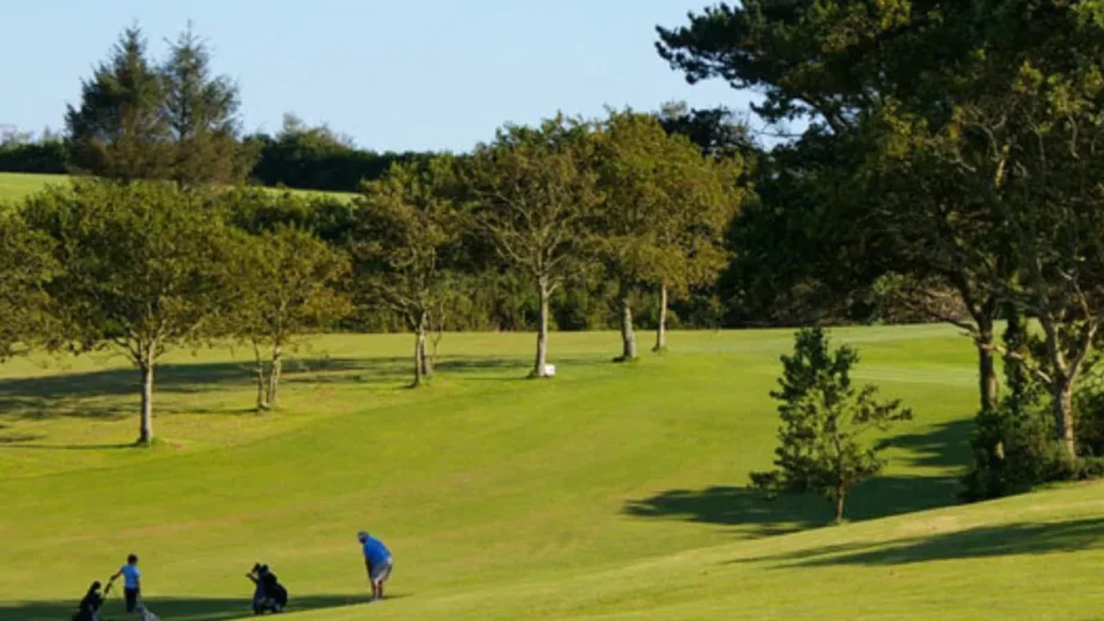 Fairway vallonné et arboré du Golf de Brest les Abers, avec plusieurs golfeurs au départ.
