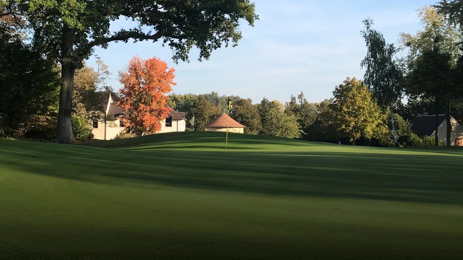Green du Golf de l’Isle Adam entouré d’arbres, avec le club-house en arrière-plan.