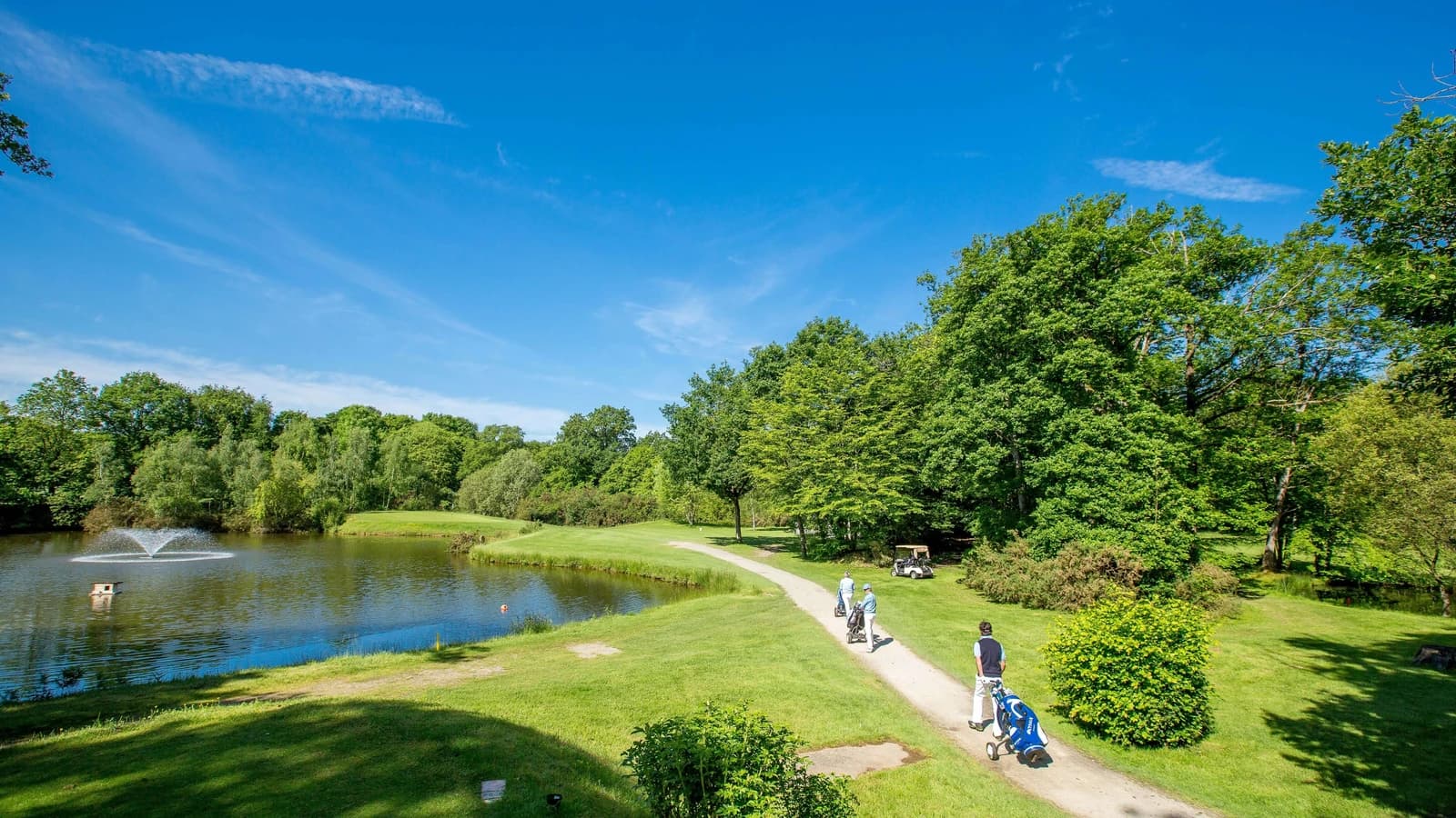 Golfeurs longeant une pièce d’eau sur le parcours boisé du Golf de la Freslonnière.