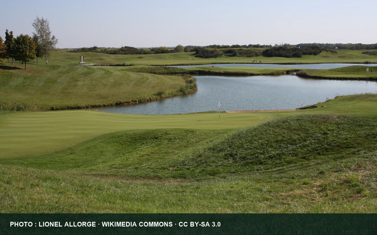 Vue du Golf National avec un green, une pièce d’eau et les ondulations du parcours.