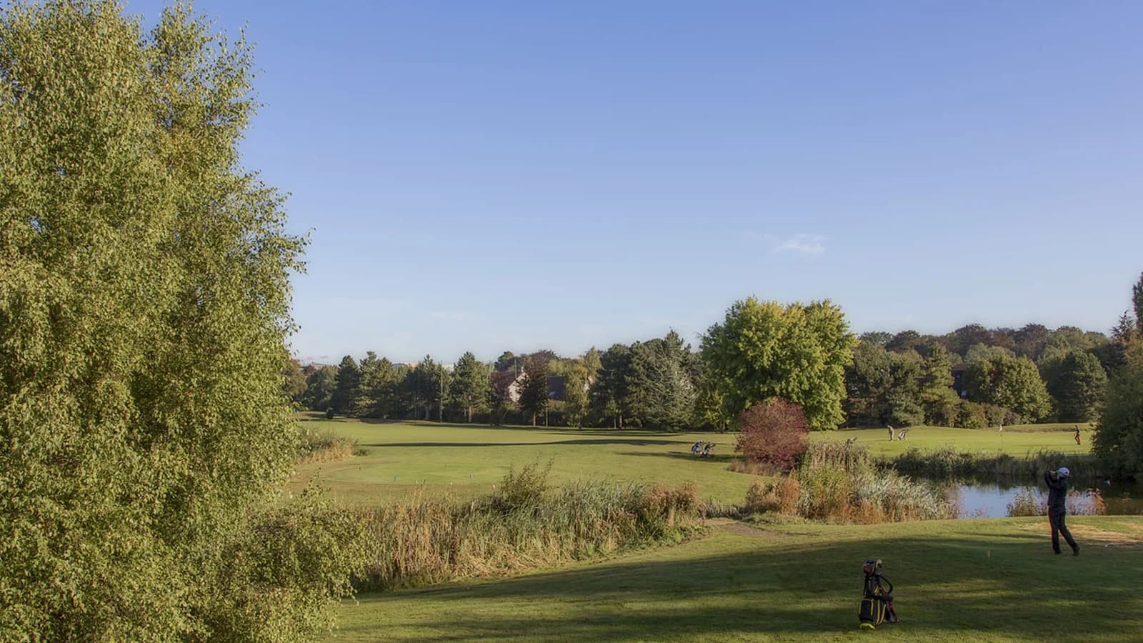 Vue du parcours UGOLF Cergy-Vauréal avec fairway, plan d’eau et arbres.