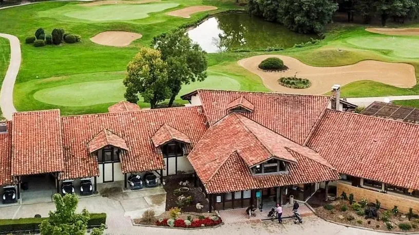 Vue aérienne oblique du club-house entouré des greens et bunkers.