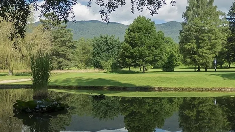 Green au-delà d’un plan d’eau et arbres, montagnes au fond.