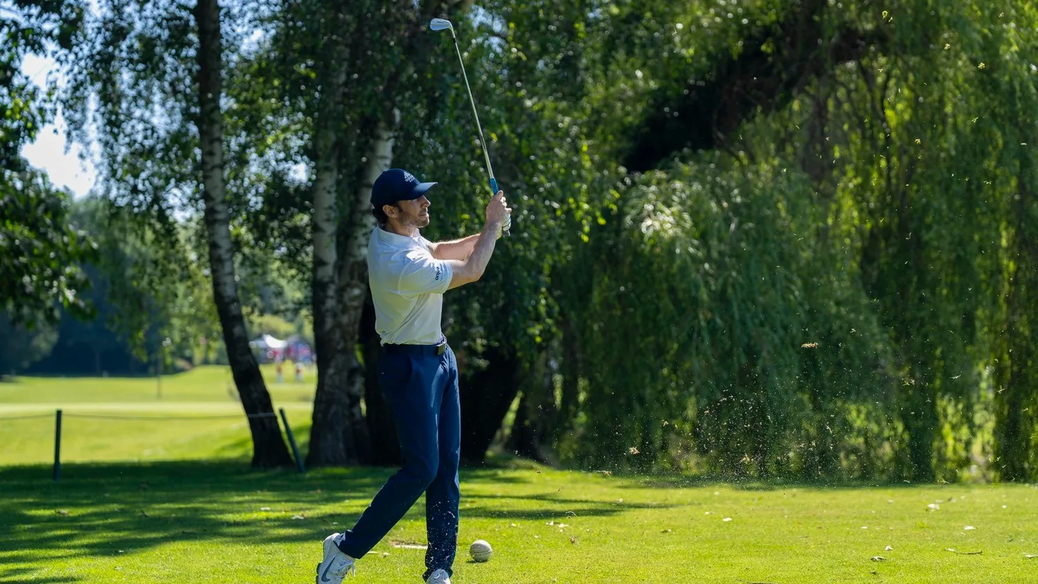 Golfeur en plein swing sur le parcours arboré.