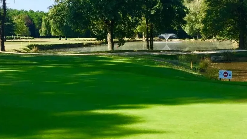 Green ombragé avec drapeau et plan d’eau.