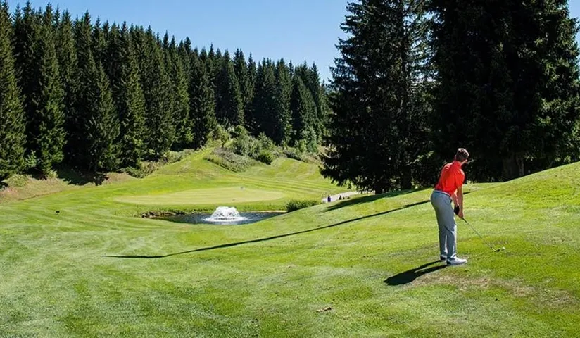 Golfeur de dos sur le parcours du golf des Gets bordé de conifères.